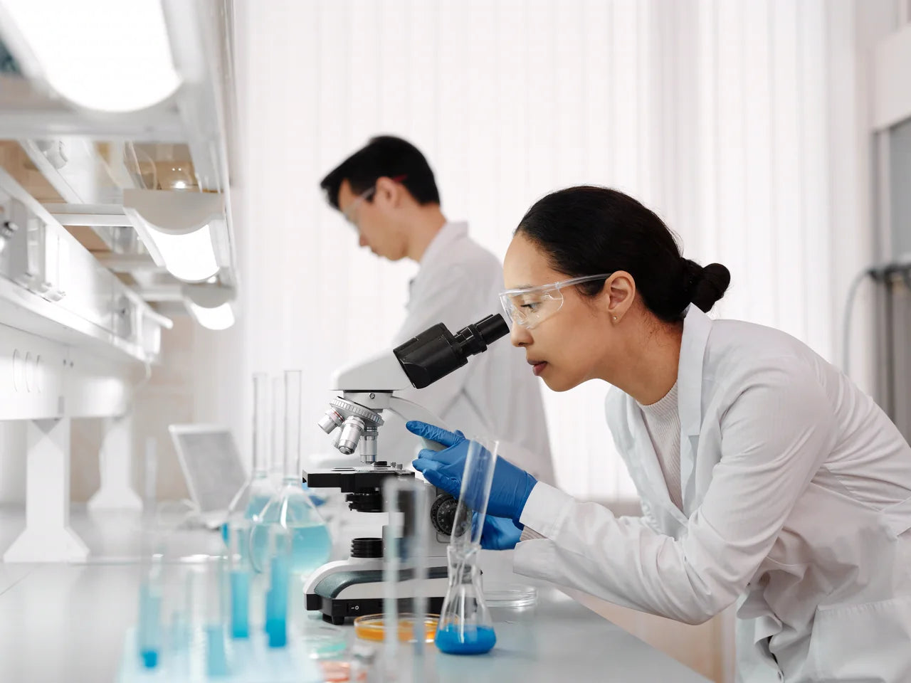 Two researchers at a laboratory bench, one working at a microscope